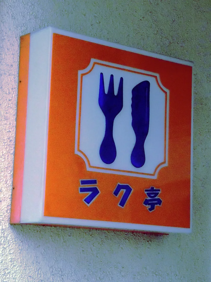 Blue fork and knife silhouettes decorate an orange square sign on a pale wall.