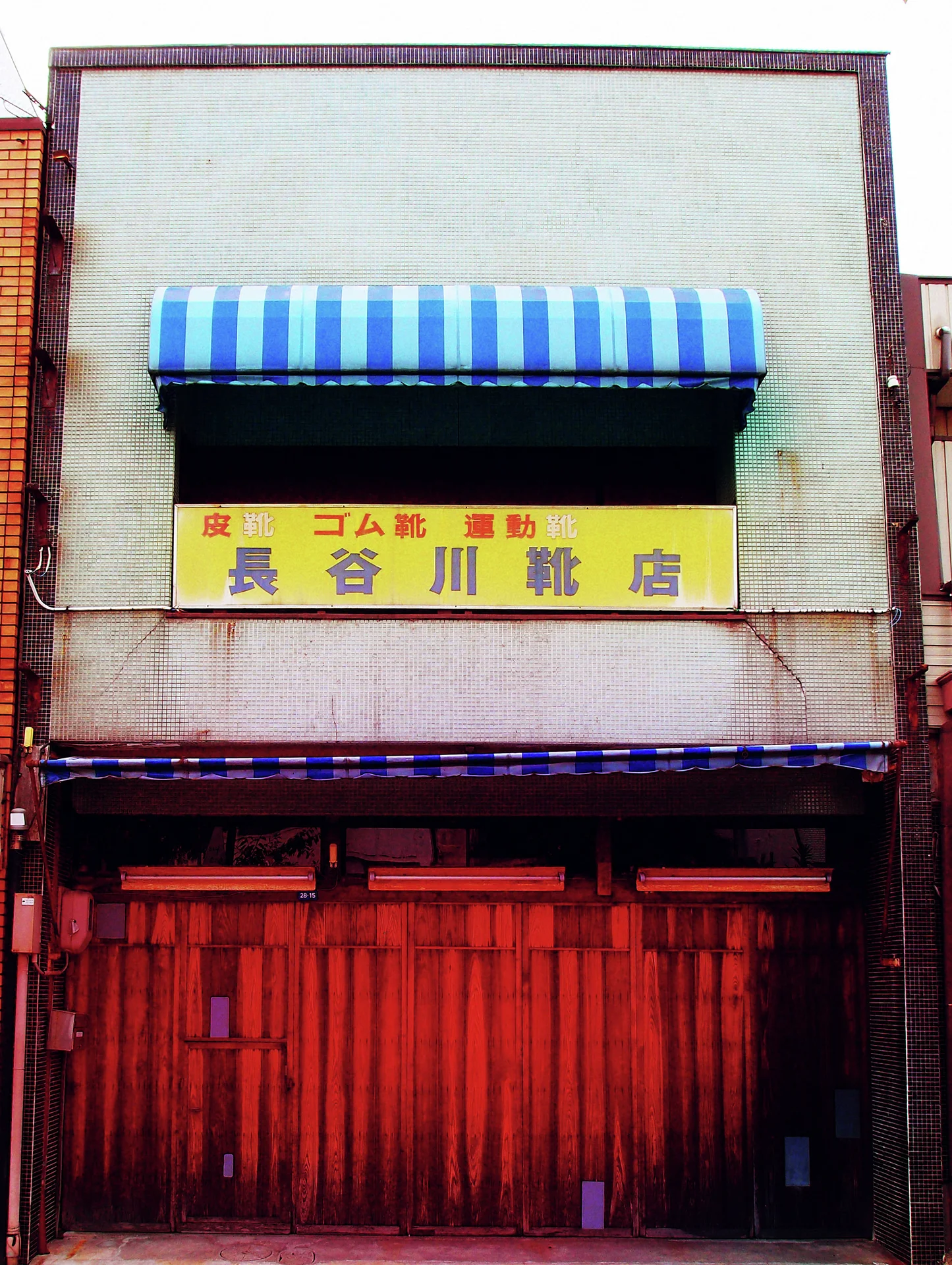 A blue striped awning shades a yellow sign above a closed red wooden storefront.
