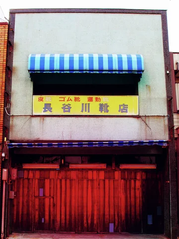 A blue striped awning shades a yellow sign above a closed red wooden storefront.
