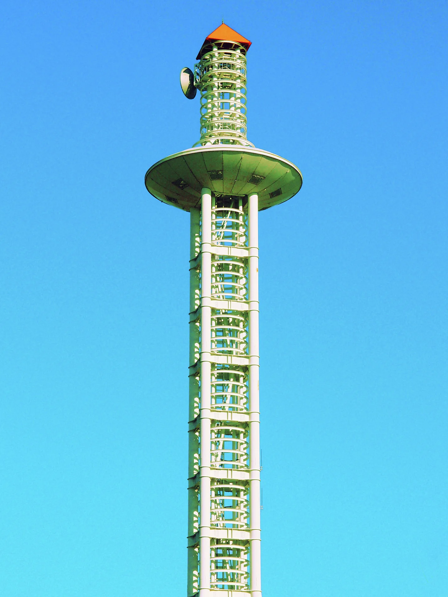 A tall lattice tower with a broad circular platform and orange cap rises against clear blue sky.