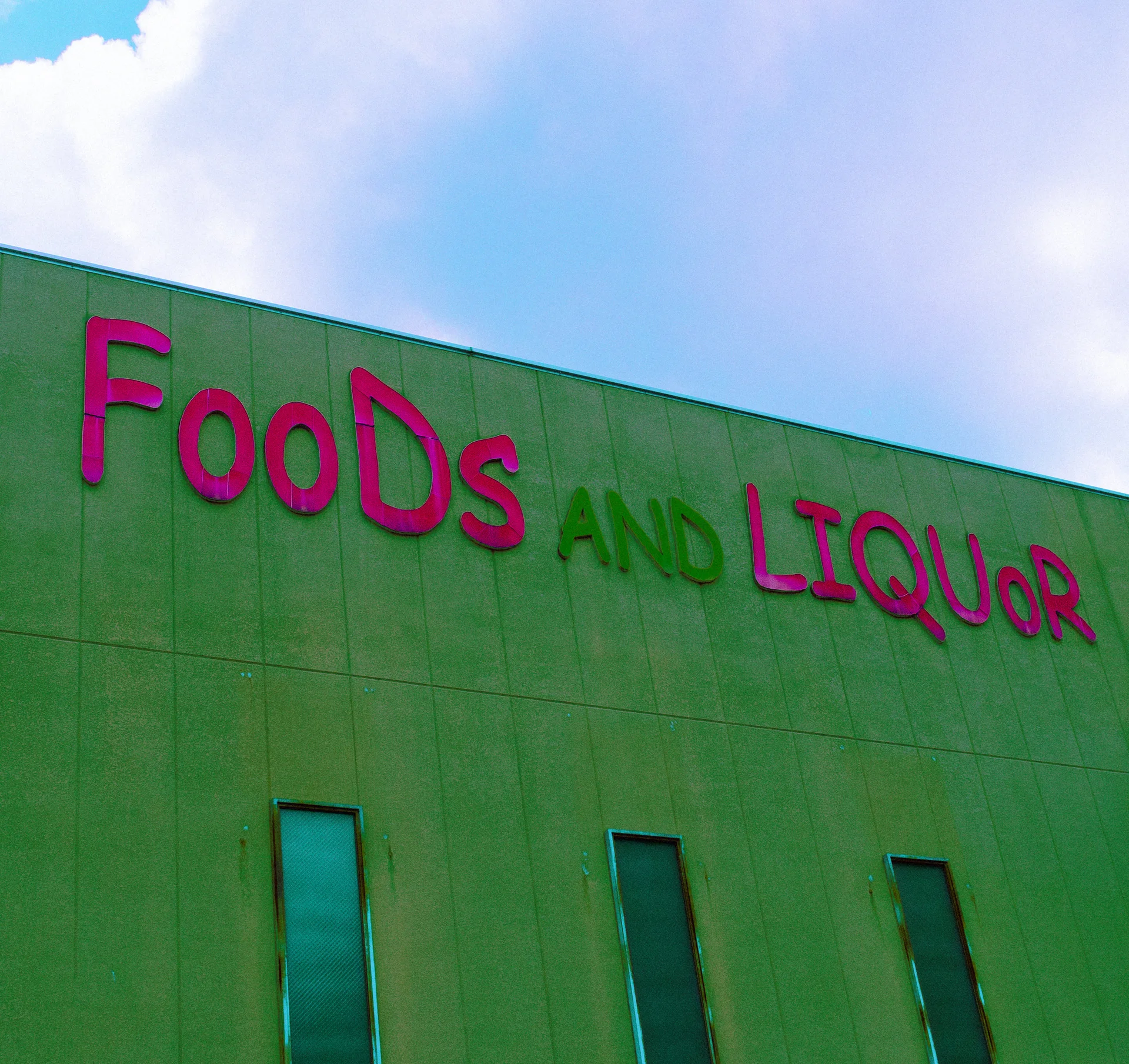 Pink Foods and Liquor lettering runs across a green building facade beneath pale blue clouds.
