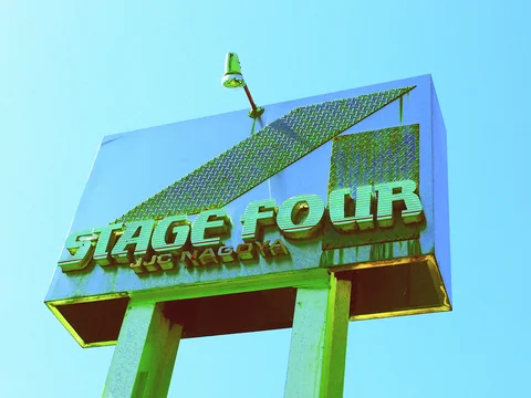 Raised Stage Four lettering decorates a tall pale sign with geometric panels beneath a single small lamp.
