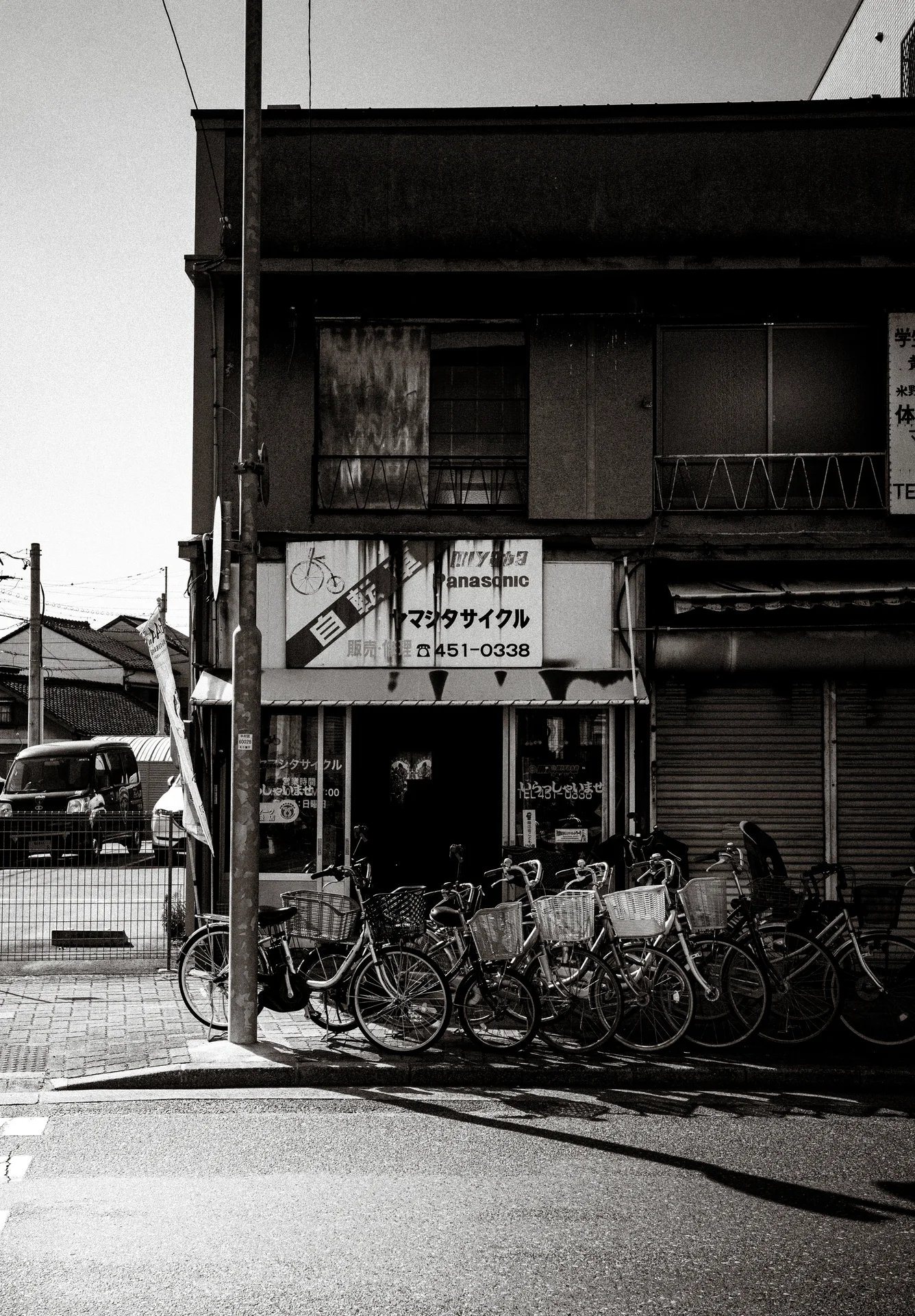 A row of bicycles crowds a weathered corner shop beneath faded signs in monochrome.