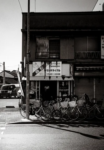 A row of bicycles crowds a weathered corner shop beneath faded signs in monochrome.