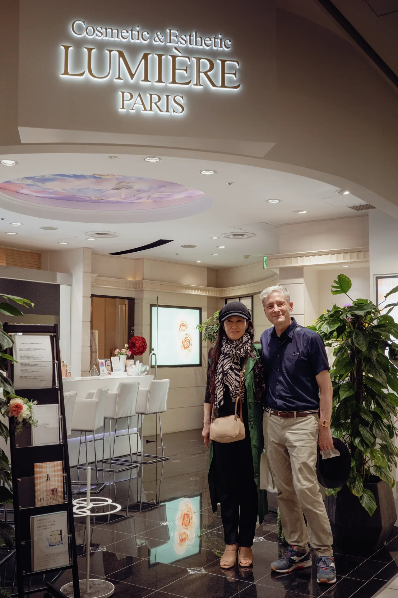 Two adults stand beneath illuminated salon lettering inside a curved entrance with glossy floor tiles.