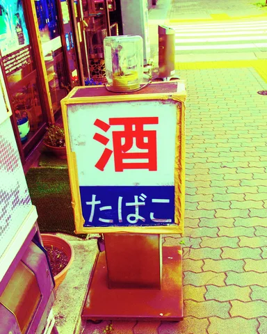A small freestanding sign bears a large red character above blue lettering on a brick sidewalk.