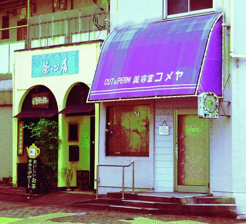A purple curved awning shades a narrow storefront beside an entrance with paired dark semicircular arches.