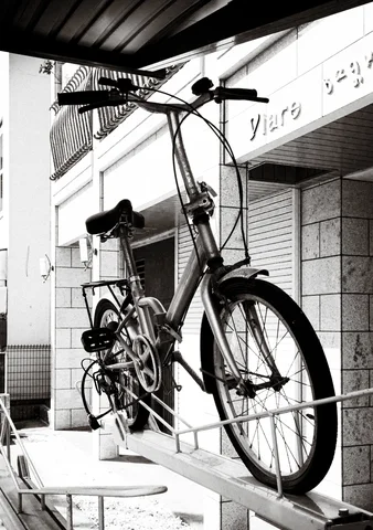 A bicycle rests on a raised ledge beneath an awning above pale chairs in black and white.