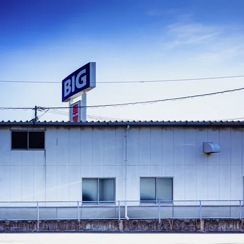 A BIG sign rises above a low white building beneath blue sky and overhead wires.