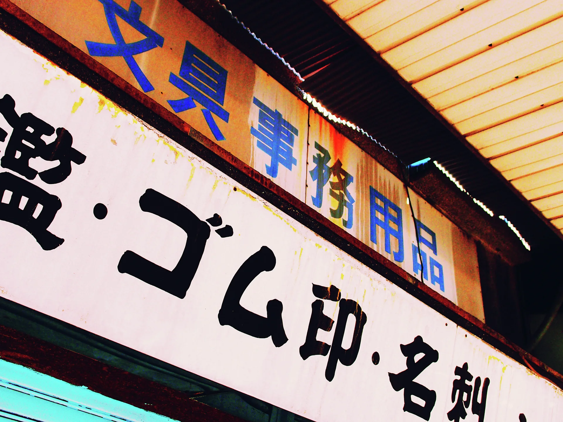 Japanese lettering fills stacked orange and pale shop signs beneath a dark-edged translucent canopy.