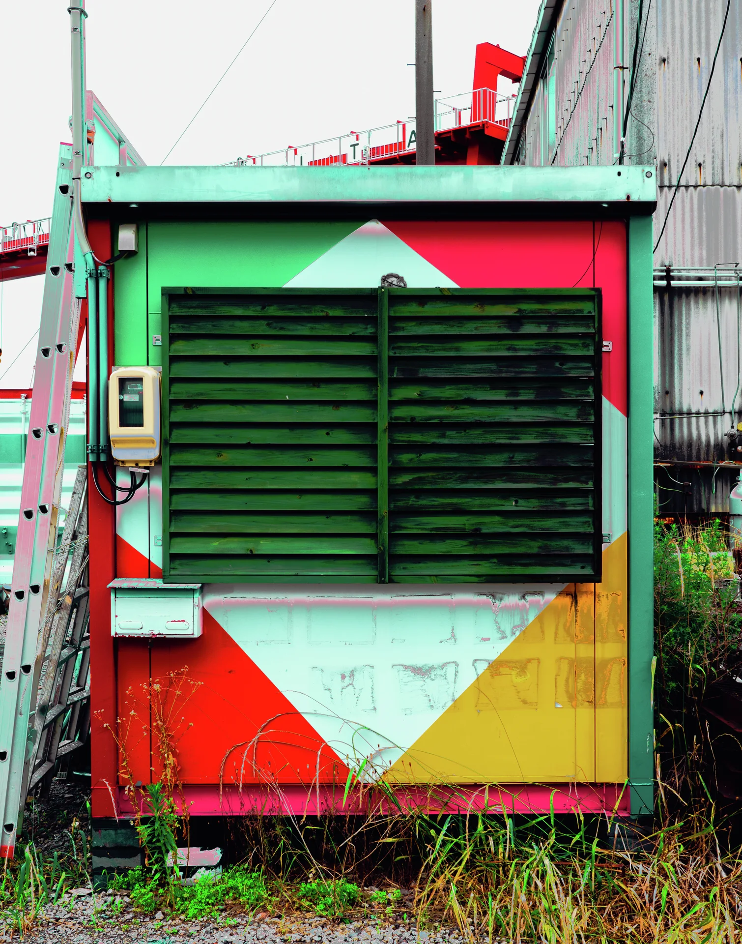 Dark green shutters cover a small structure painted with bold red, white, green, and yellow triangles.