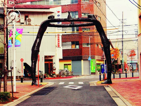 A dark irregular arch spans a small urban street above brick sidewalks and white road markings.