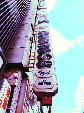 A tall directory with stacked rounded business labels rises beside a building in a steep upward view.