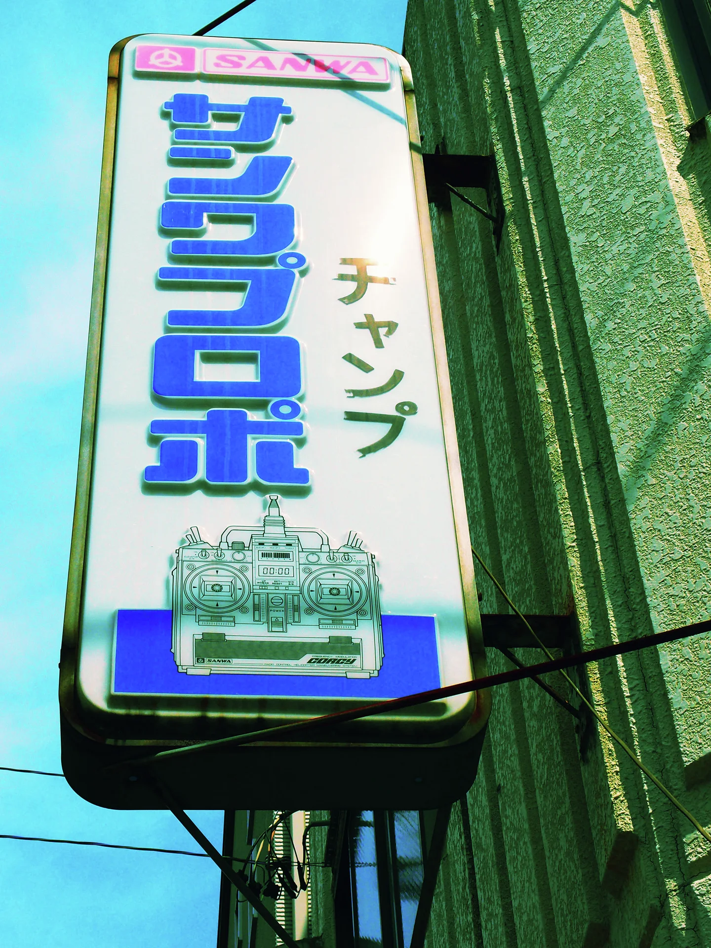 Bold blue characters and an illustrated machine fill a projecting white vertical sign.