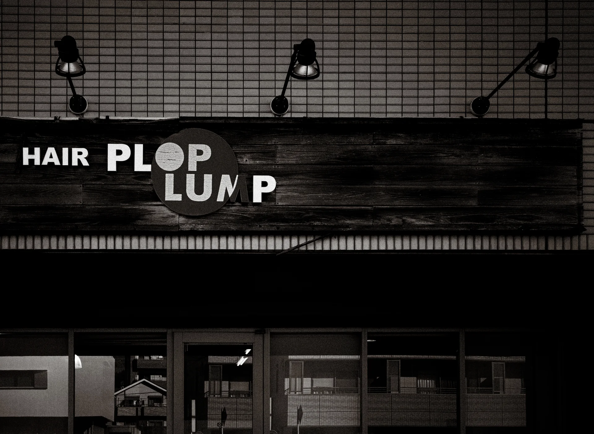 Three angled lamps illuminate a hair salon sign above glass doors in black and white.