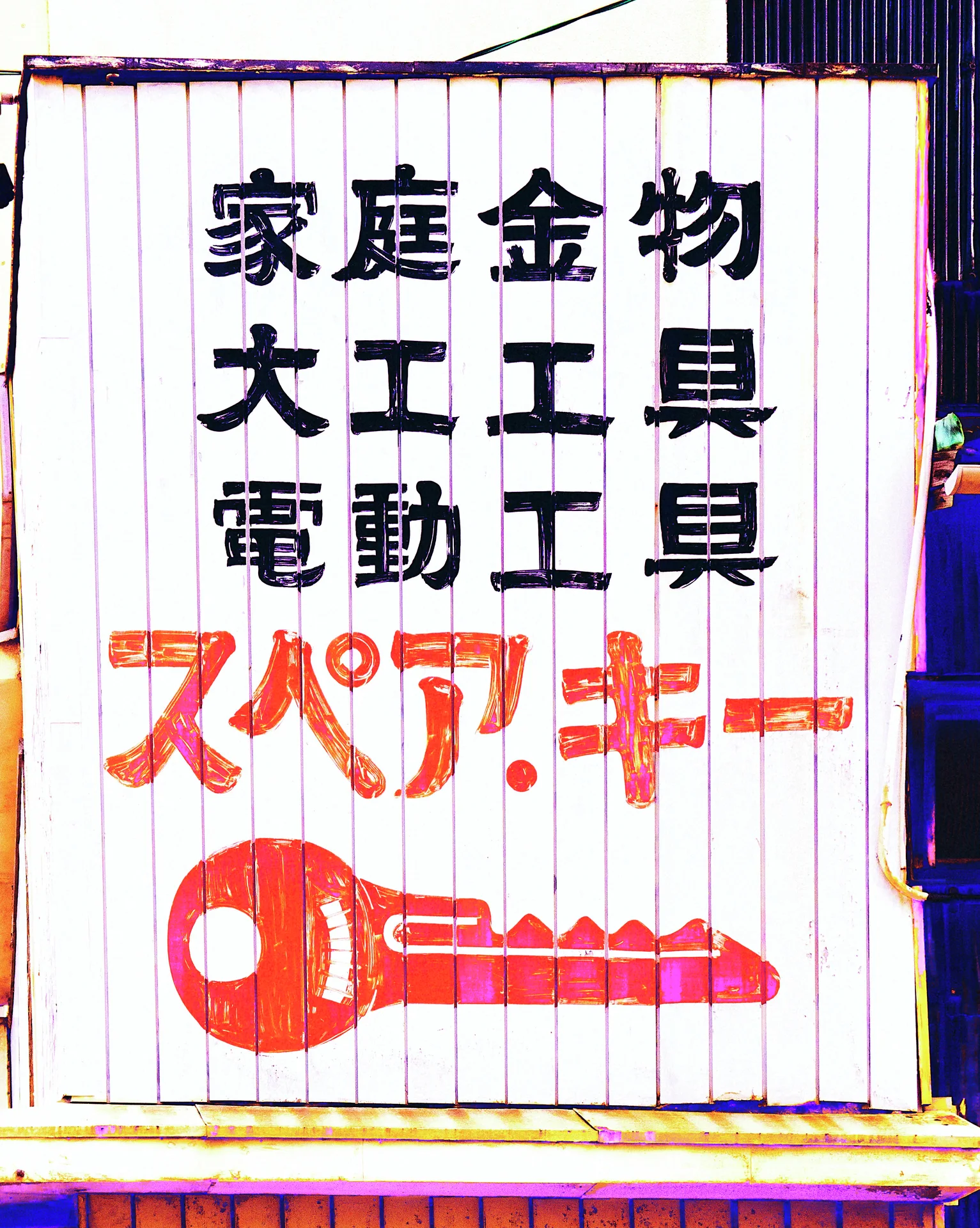 Black and red Japanese lettering and a large red key decorate a white corrugated shop sign.