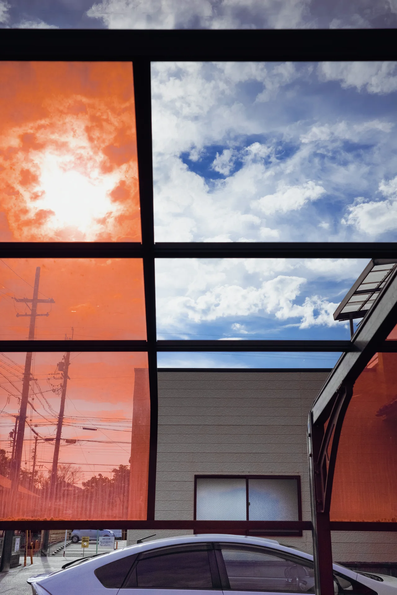 Dark window frames divide orange-tinted panes and reflections of blue sky and white clouds.