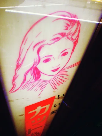 A pink illustrated woman's face fills a pale vertical sign behind reflective glass.