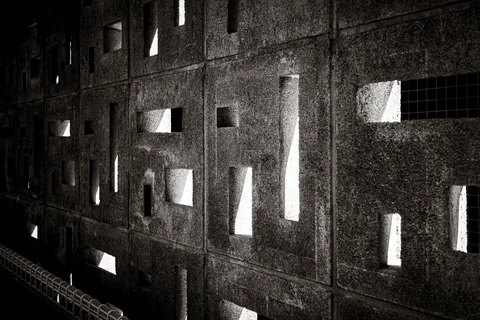 Sunlight passes through irregular rectangular openings in a dark concrete block wall in black and white.