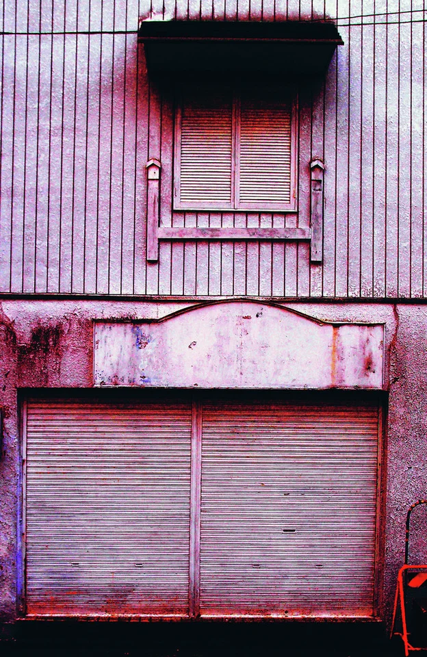 A small shuttered upper window sits above closed shop shutters on a pink weathered facade.