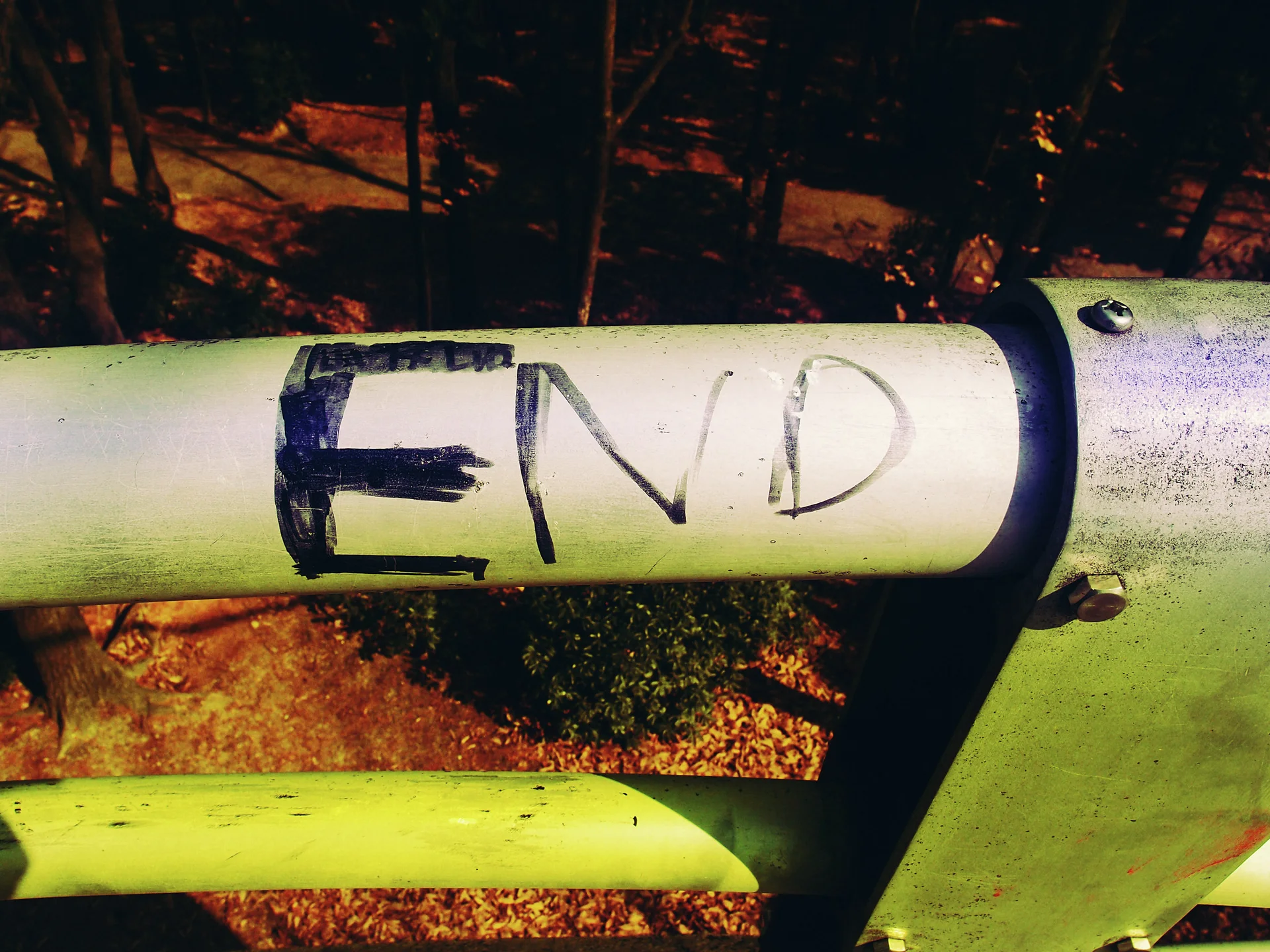 The handwritten word END appears on a pale metal railing above a sunlit wooded slope.