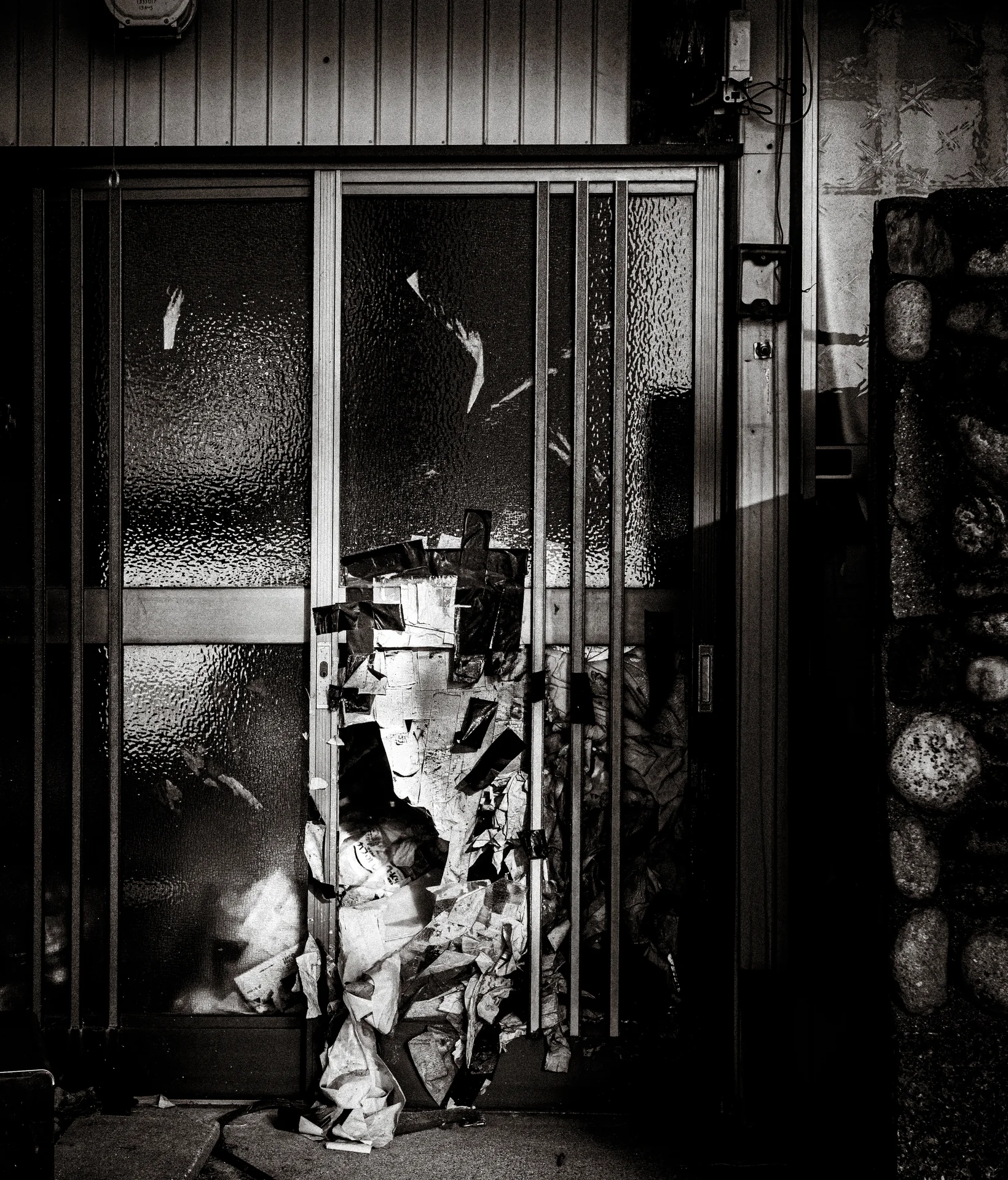 Torn pale covering hangs before textured glass doors and vertical metal bars in black and white.