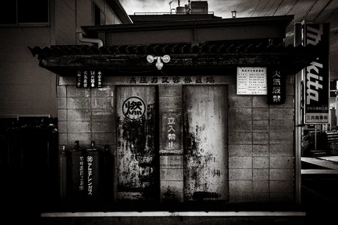 Weathered metal doors beneath a tiled canopy fill a shadowy storefront in black and white.