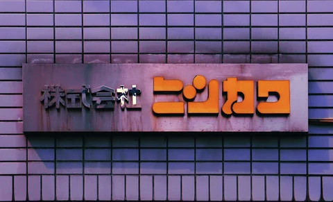 Raised orange Japanese lettering and smaller dark characters sit on a gray plaque against square wall tiles.