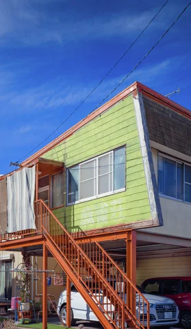 Orange outdoor stairs climb to the upper floor of a pale green building beneath blue sky.