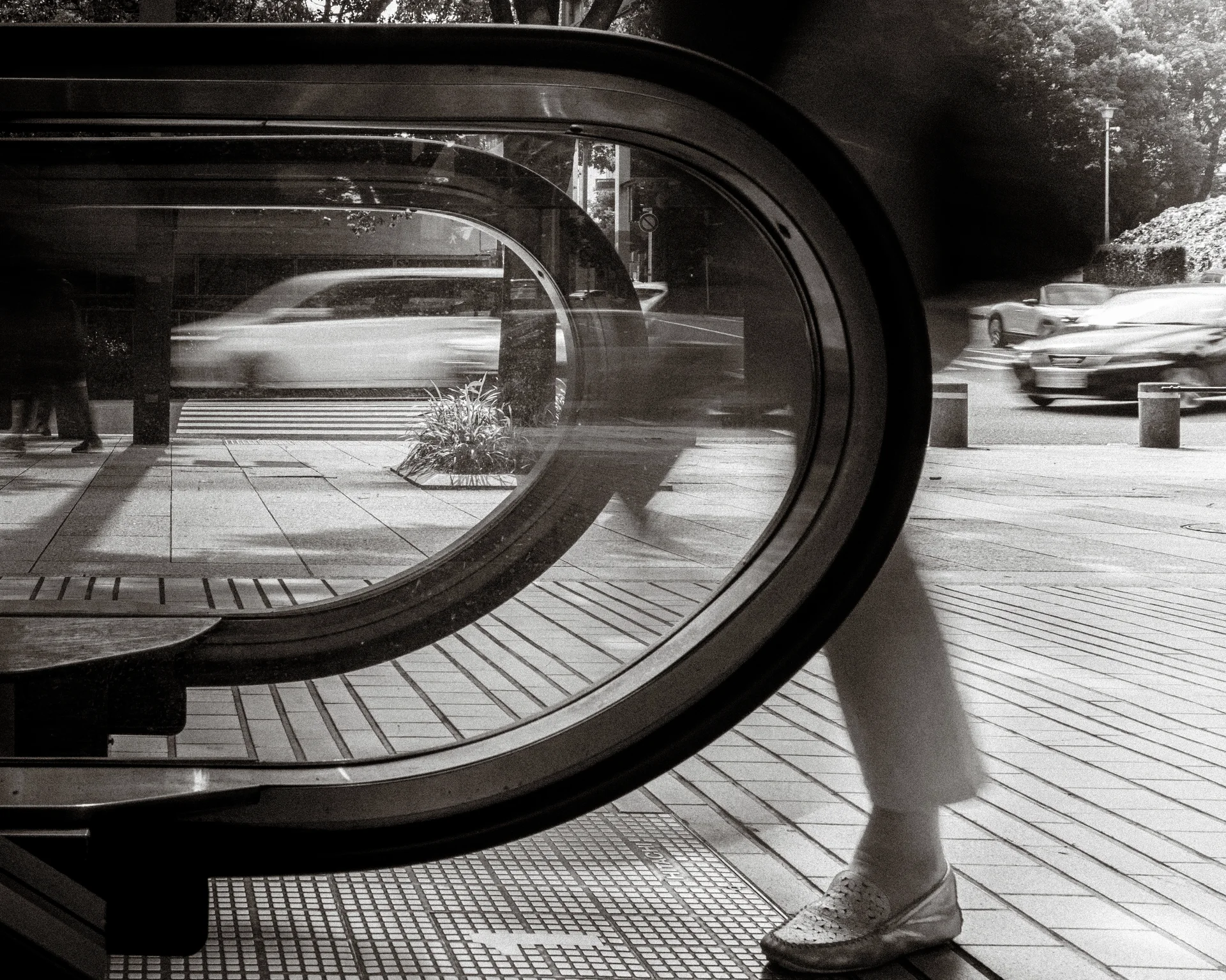 Nested curved window frames overlay a blurred pedestrian and passing cars in black and white.