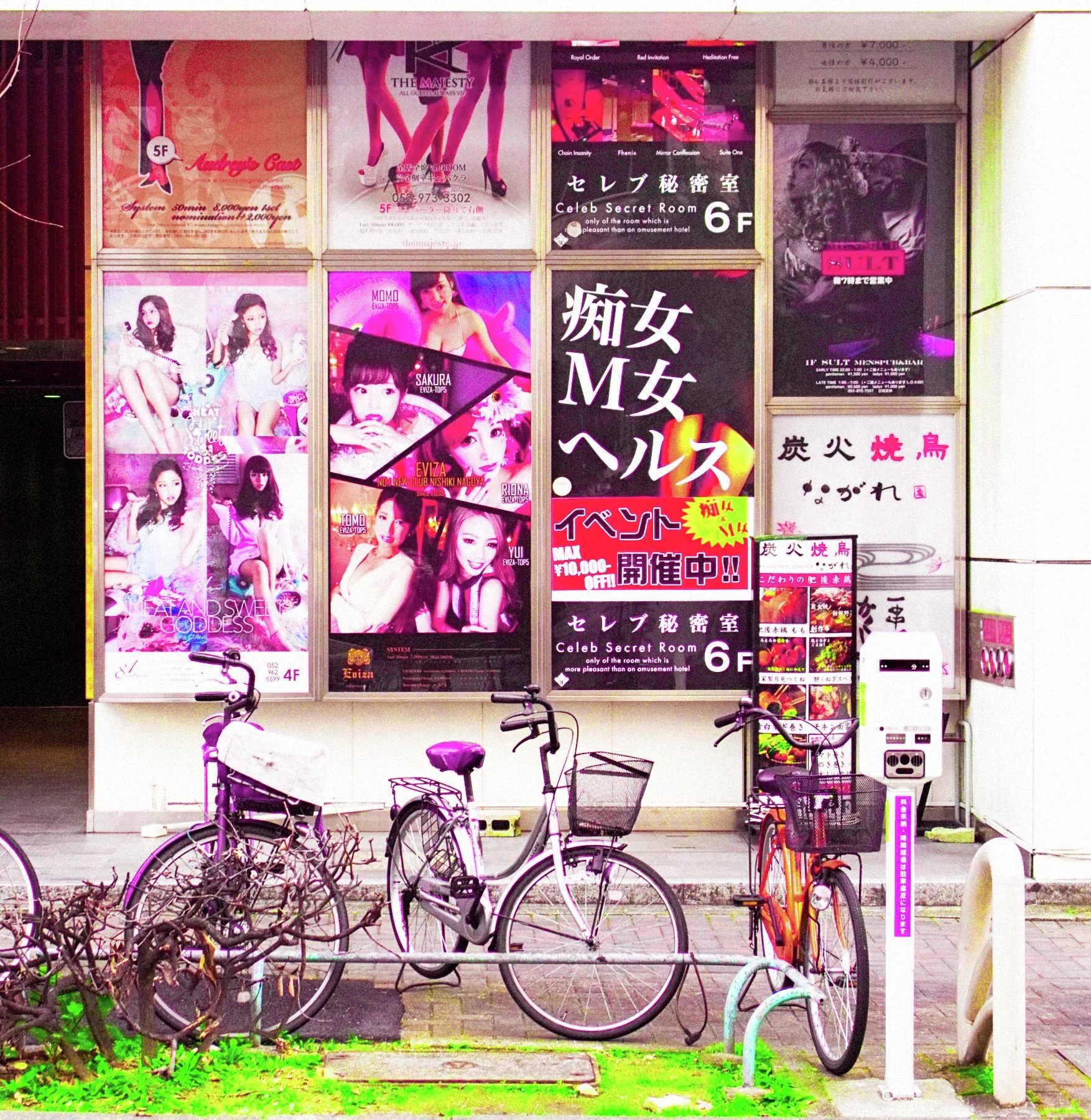 Parked bicycles stand below a dense wall of colorful advertisements with portraits and Japanese lettering.