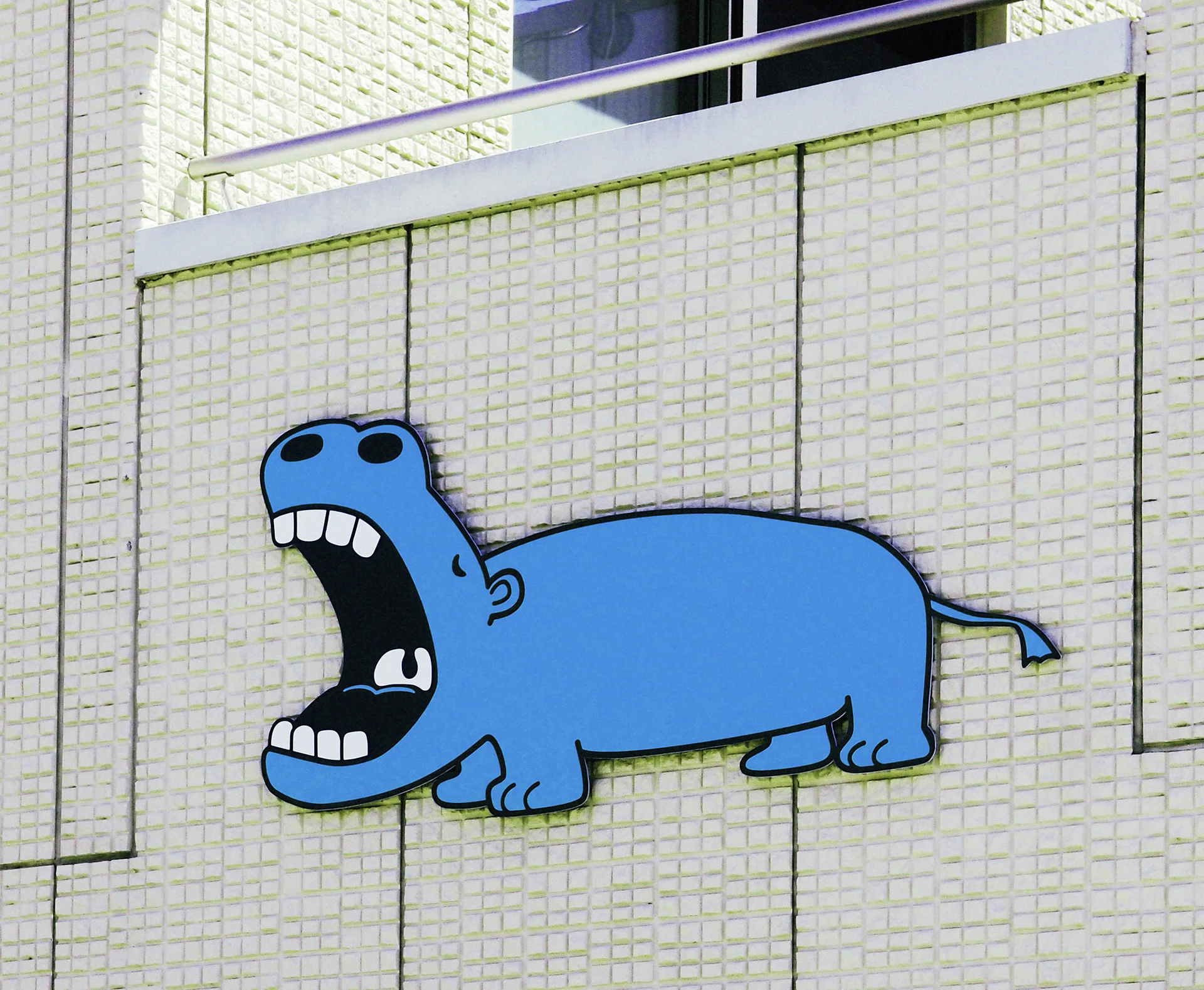 A cartoon blue hippopotamus with a wide open mouth decorates a pale tiled wall.