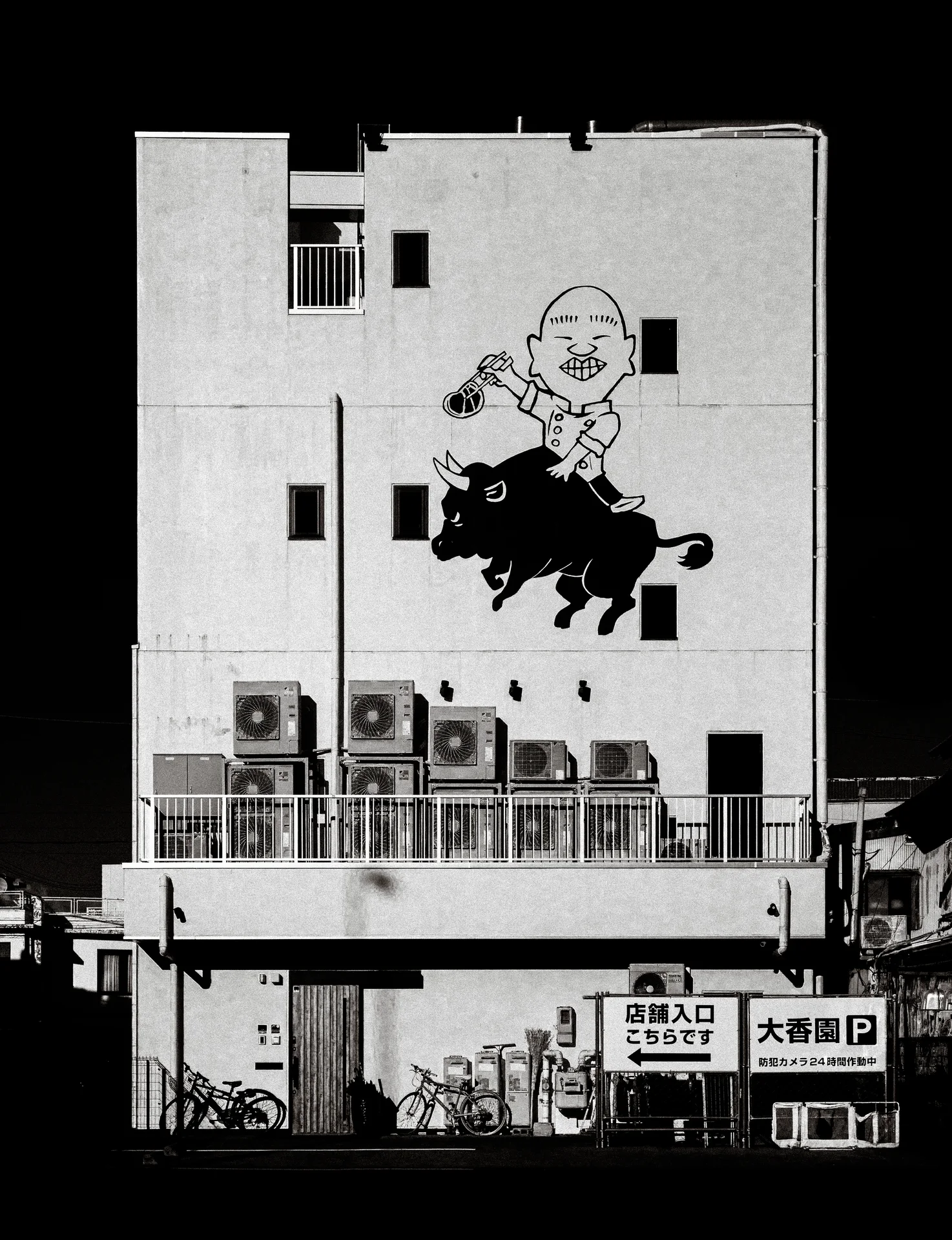 A cartoon rider on a bull decorates a pale building wall above outdoor equipment in black and white.