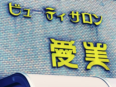 Raised yellow salon characters cast blue shadows across a wall of small pale tiles.