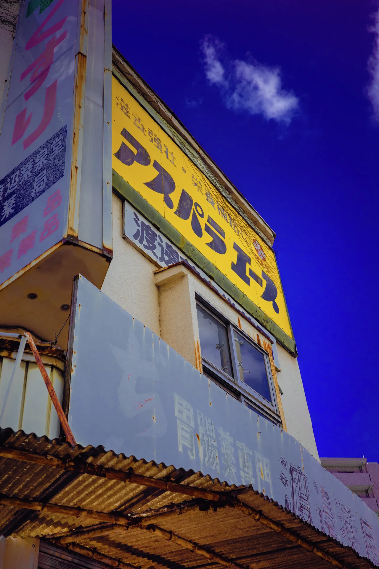 A large yellow Japanese sign crowns an aging building above a rusty corrugated awning.