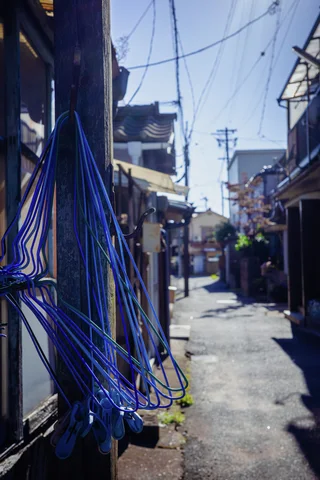 Blue hoses hang beside a utility pole along a narrow residential lane crossed by overhead wires.