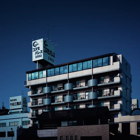 A multi-story building displays repeated curved balconies and blue upper windows beneath a rooftop sign.
