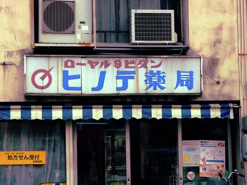 Two air conditioners sit above a pharmacy sign and blue-and-white striped storefront awning.