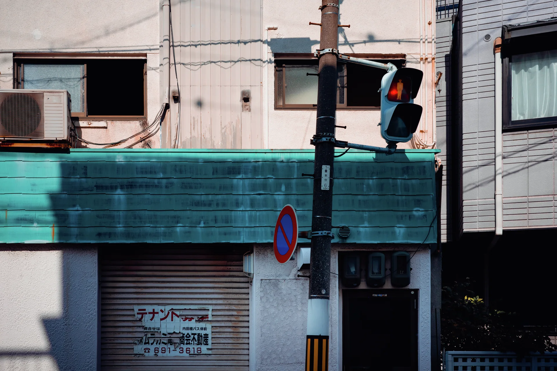 A turquoise awning spans a shuttered storefront beside a traffic signal showing red.