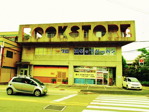 Large cutout Book Store lettering tops a low building beside passing cars and a striped pedestrian crossing.
