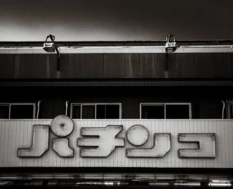 Large raised Japanese lettering spans a building facade beneath two lamps in a black and white view.