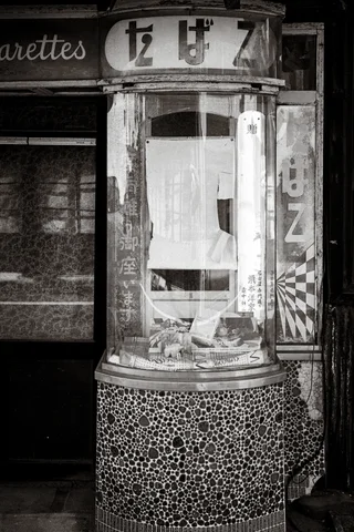 A rounded glass display case stands above mosaic tiles outside an old shop in monochrome.