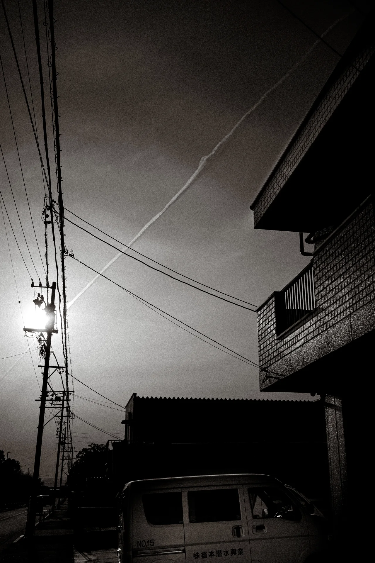 The low sun shines beside utility wires and a silhouetted building above a partly visible van.
