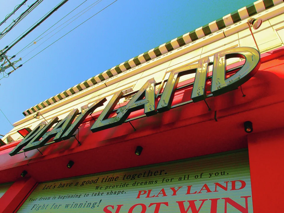 Raised metallic PLAY LAND lettering spans a vivid red building fascia beneath blue sky.