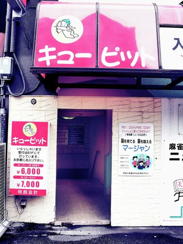 A pink sign and price board mark a pale building entrance with a dark corridor.
