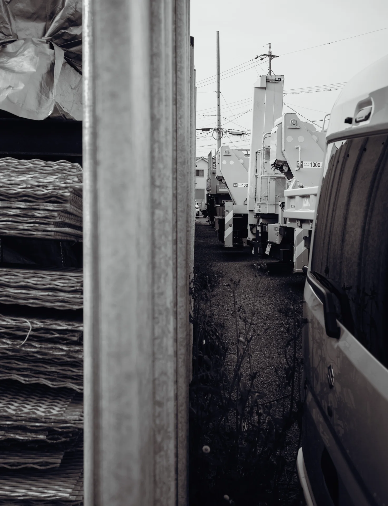 A metal post separates stacked materials from a parked van along a narrow black and white passage.