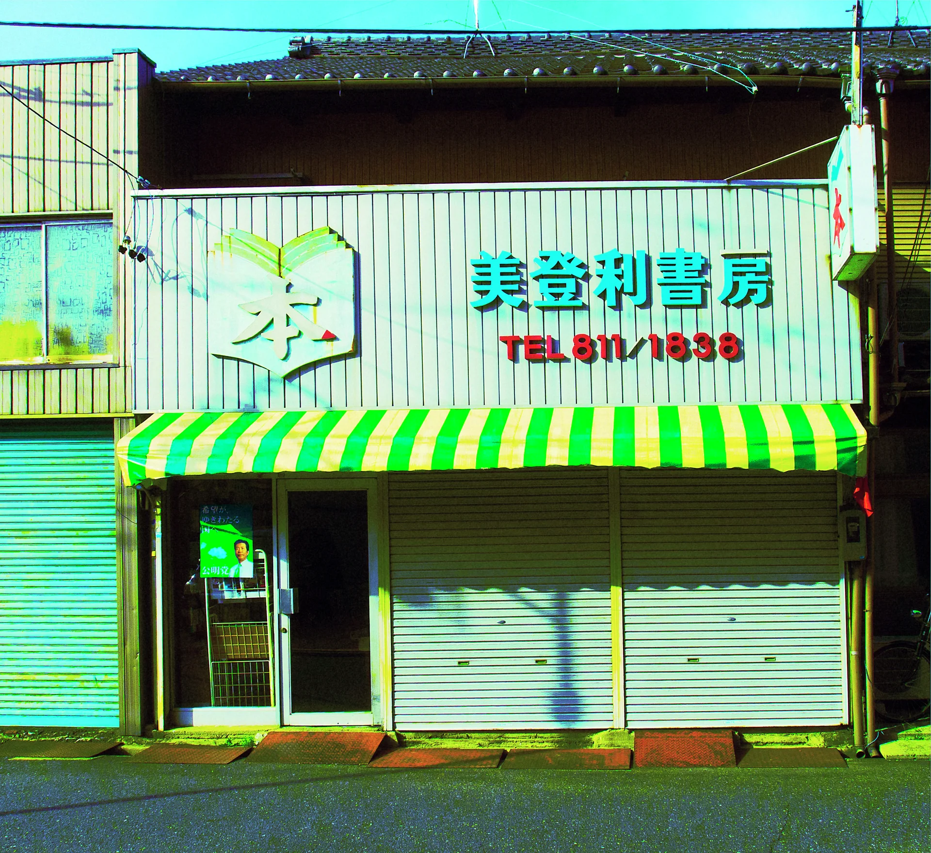 A green-and-yellow striped awning shades closed shutters beneath raised turquoise characters and red barber lettering.