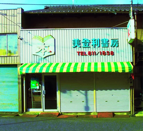 A green-and-yellow striped awning shades closed shutters beneath raised turquoise characters and red barber lettering.
