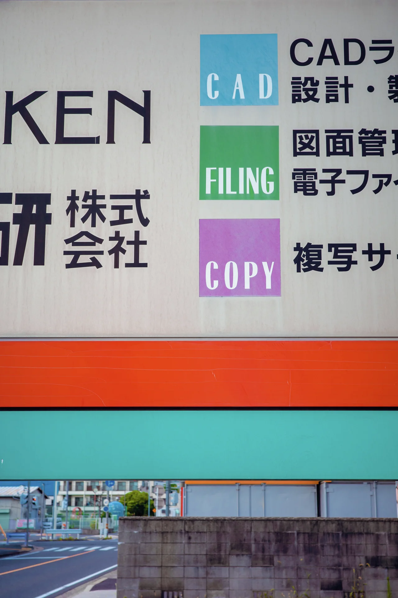 A large sign combines Japanese lettering and three colored English labels above orange and turquoise horizontal bands.