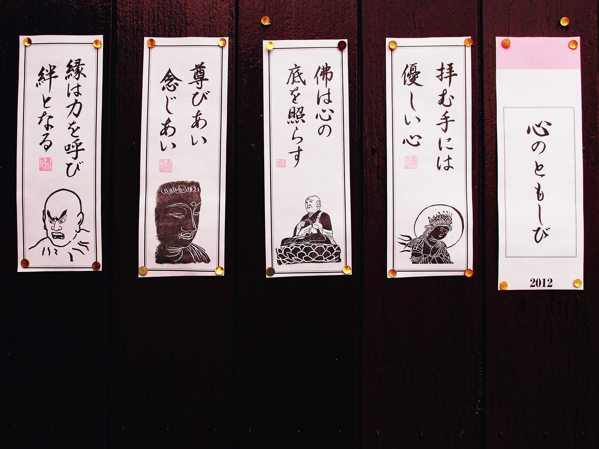 Five narrow paper notices with Japanese calligraphy and small illustrations hang against a dark wooden wall.